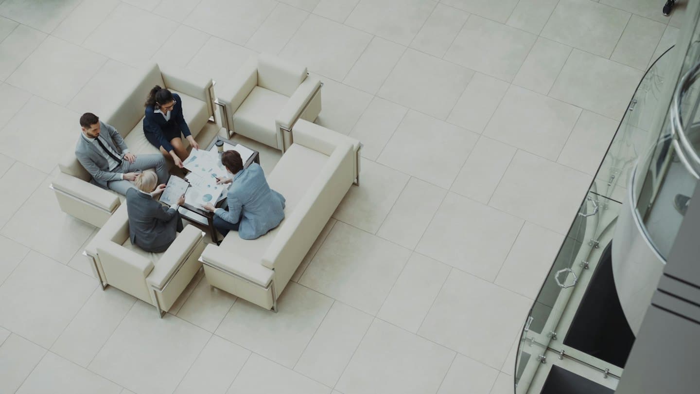 Four professionals in an office lobby reviewing documents around a table.